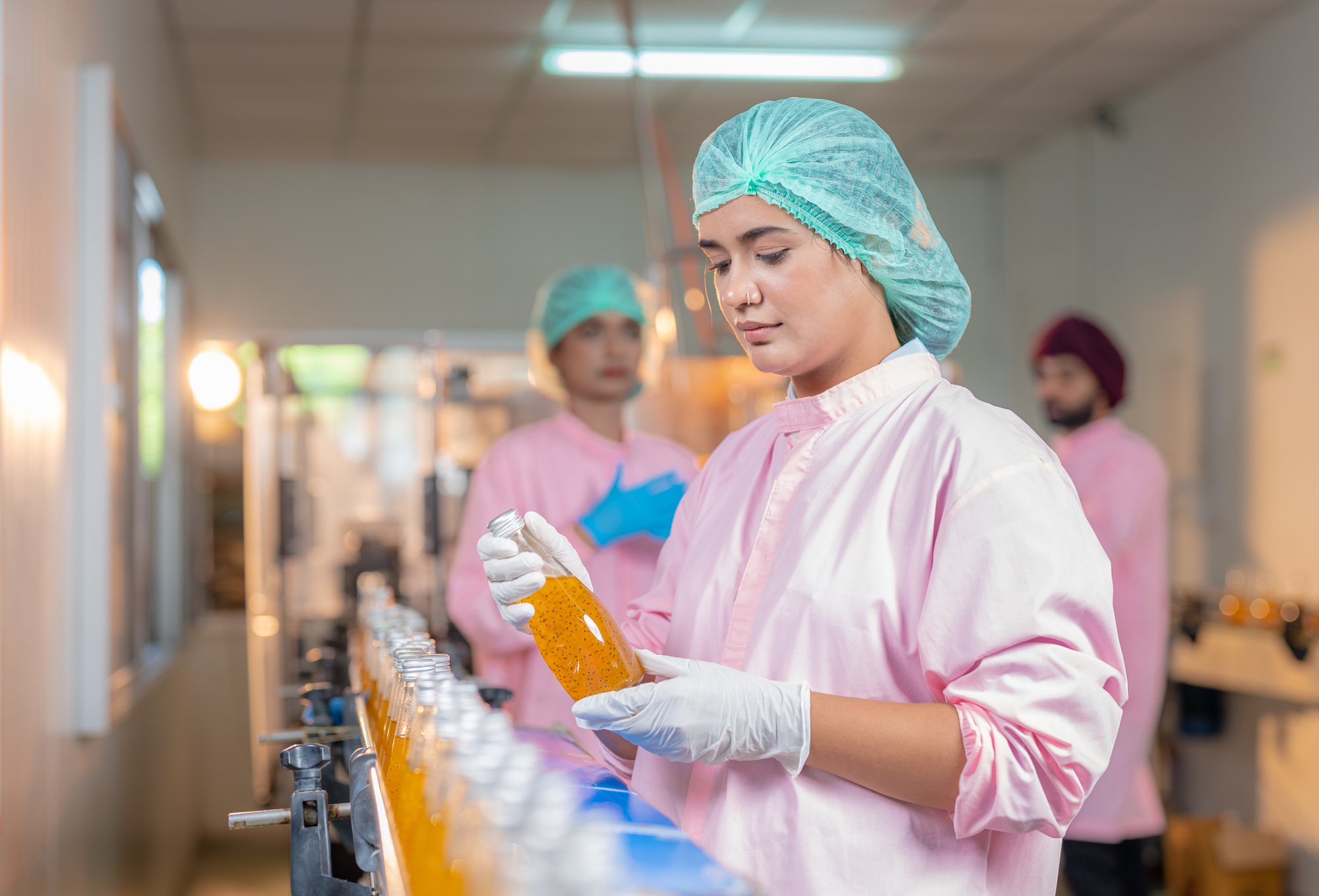 Female employee worker in uniform checking quality of fruit juice drinks bottle in production line food and beverage factory industry