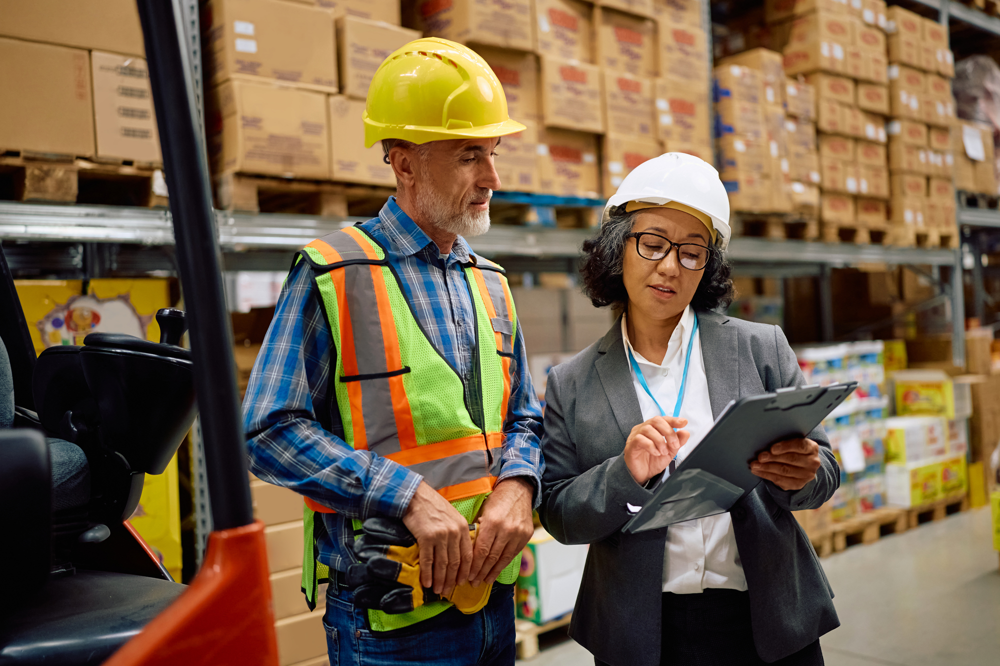 Mature businesswoman and warehouse foreman going through checklist in a storage compartment.